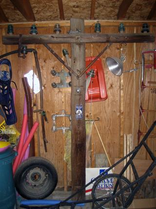 Single cross-arm pole.  3 pins on each side of arm.  Metal braces come down to pole and screw in.  This is a slightly larger arm than was on previously, so braces go down to a second bolt hole, not the original. Cross arm taken from a downed pole just a couple from where the pole came from.  Adorned with 2 side pins, a transposition bracket, and a Bell System Underground Telephone Cable sign.

Sawn off at the base almost perfectly flat -- stands on it