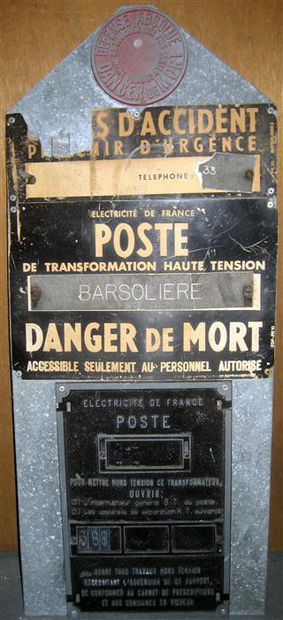 Mostly rectangular sheet of metal with a triangular top.  On this are mounted 3 different signs.

TOP (cast metal, red coated):
DEFENSE ABSOLUE / DE TOUCHER AUX FILS / / MEME TOMBER A TERRE / DANGER DE MORT

Middle (plastic, black and white, with additional mounted pieces)
EN CAS D